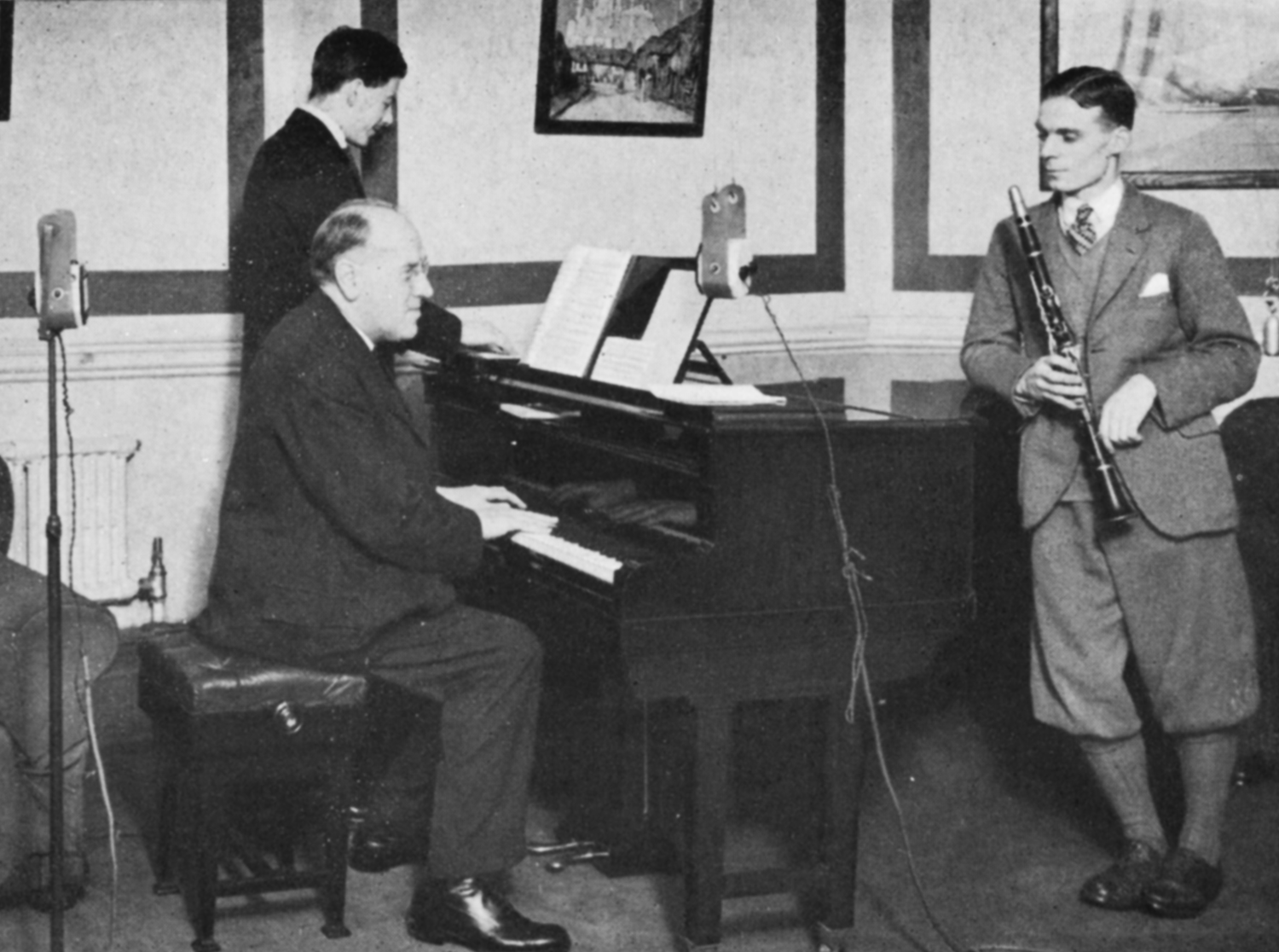 A man plays a piano as another holds an clarinet