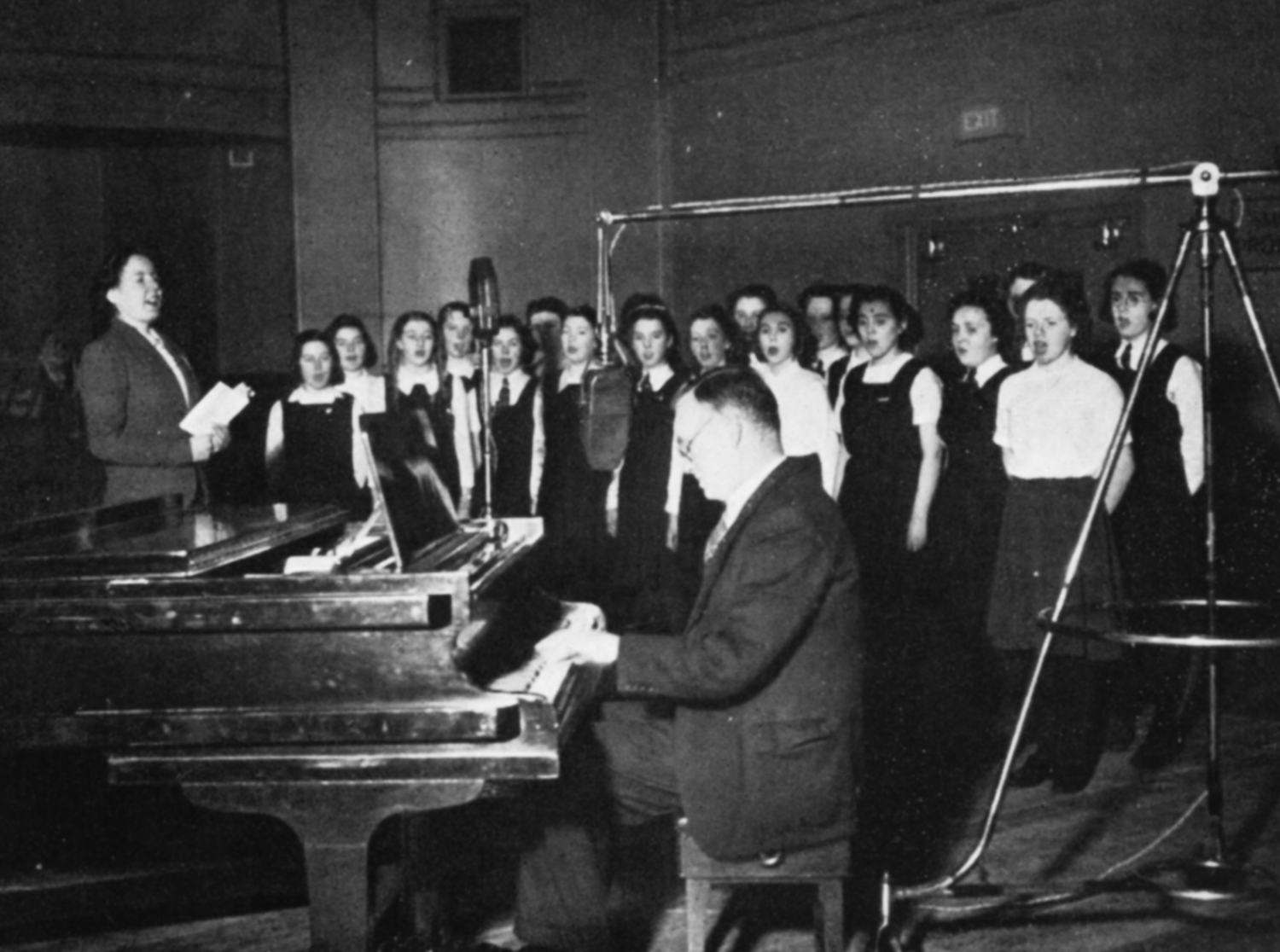 A man plays a piano with a girls' choir behind him