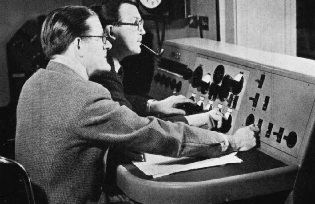Two men sit at a control panel