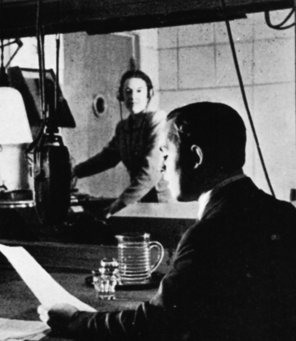 A man reads from a script whilst a woman produces from behind a window